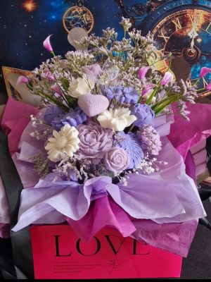 représentation d'une composition florale en bougie moulée avec feuillage et fleurs séchées dans un support carré rose avec inscription love
