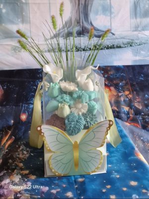 représentation d'une composition florale en bougie moulée et décor feuillage dans un contenant vert pâle décoré d'un papillon vert et doré