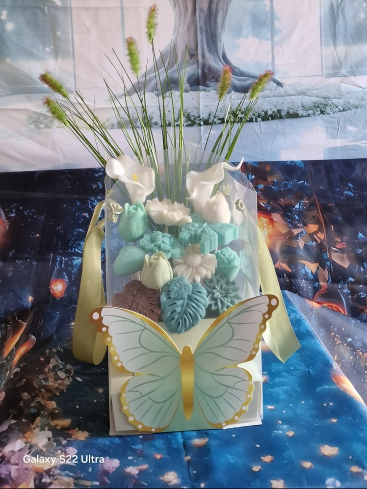 représentation d'une composition florale en bougie moulée et décor feuillage dans un contenant vert pâle décoré d'un papillon vert et doré